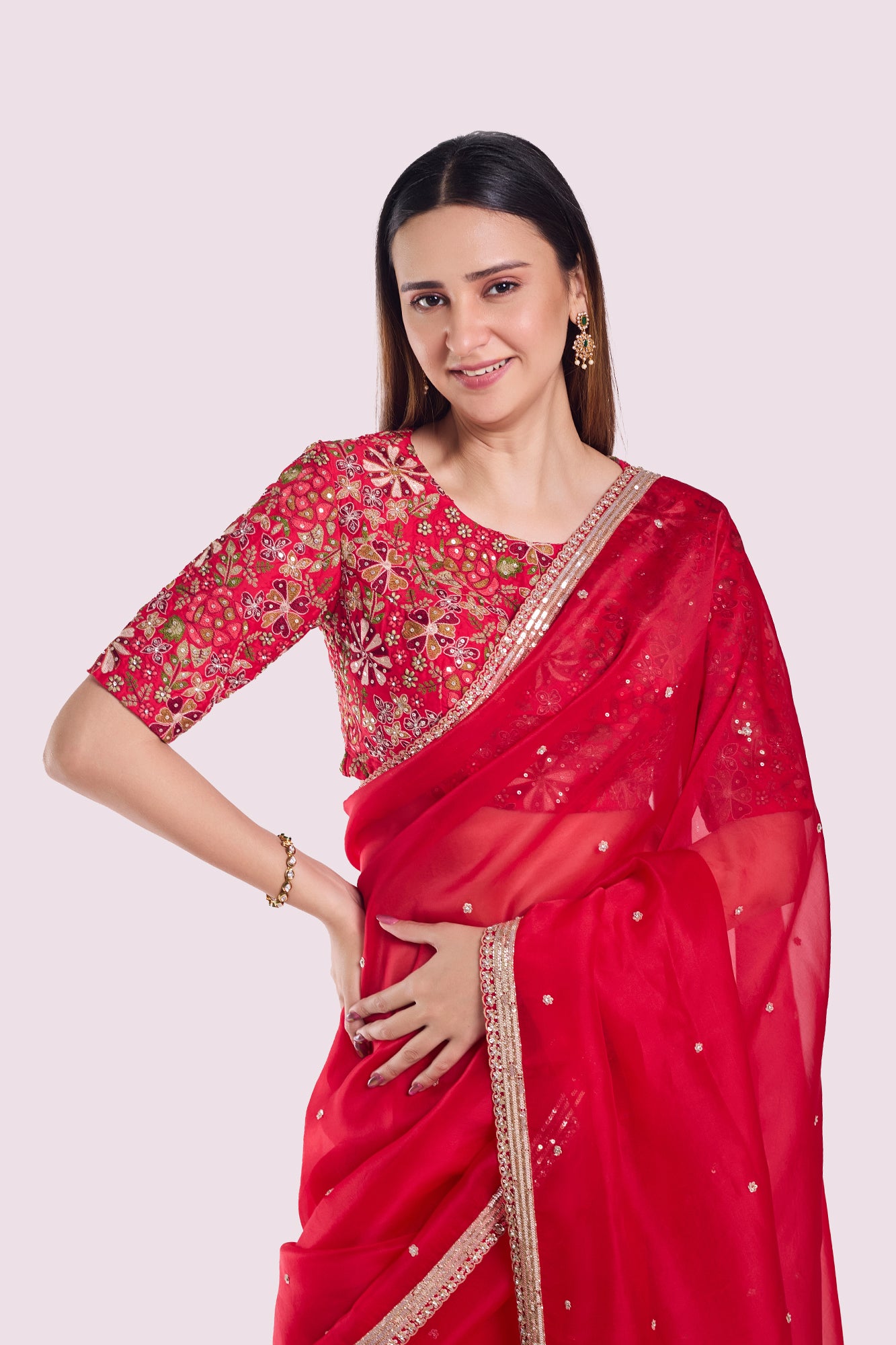 Woman wearing a red saree with gold embroidery on a light pink background